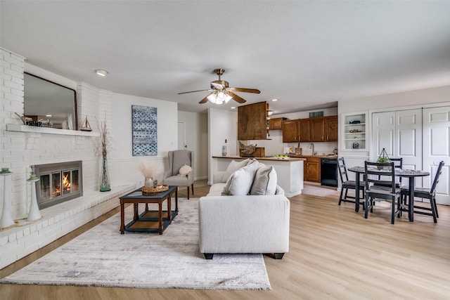 living room with ceiling fan, a brick fireplace, baseboards, recessed lighting, and light wood-style flooring