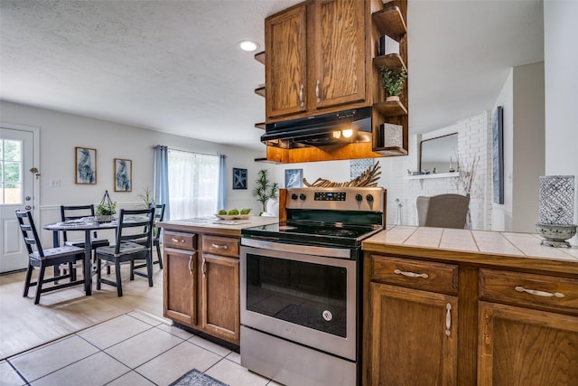 kitchen with under cabinet range hood, electric range, tile counters, and a healthy amount of sunlight