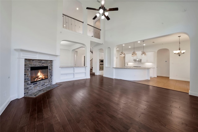 6917 Moody Ave, Frisco, TX 75035 - unfurnished living room featuring wood-type flooring, ceiling fan, arched walkways, a glass covered fireplace, and a towering ceiling