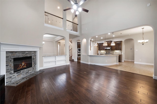 unfurnished living room with arched walkways, light wood-style floors, a fireplace, and ceiling fan with notable chandelier