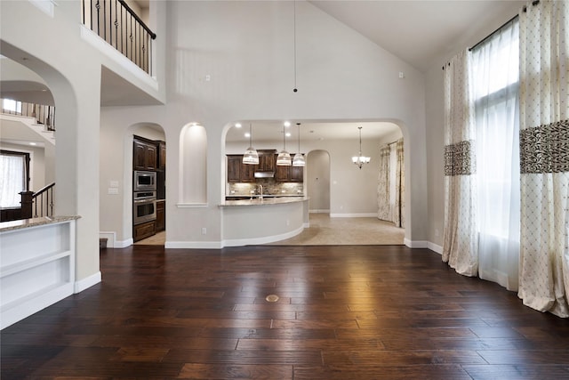 unfurnished living room featuring arched walkways, high vaulted ceiling, plenty of natural light, and hardwood / wood-style flooring