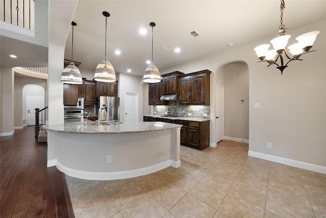 kitchen featuring dark brown cabinetry, visible vents, arched walkways, under cabinet range hood, and decorative backsplash