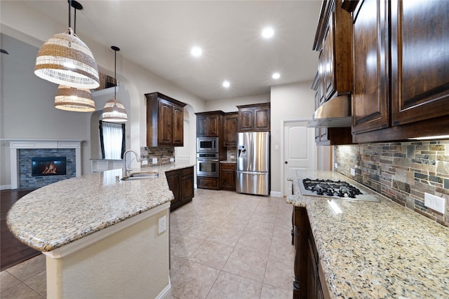 kitchen featuring dark brown cabinets, a sink, backsplash, appliances with stainless steel finishes, and light stone counters