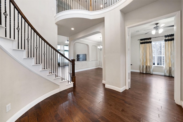 foyer entrance with a ceiling fan, wood-type flooring, a towering ceiling, arched walkways, and stairway