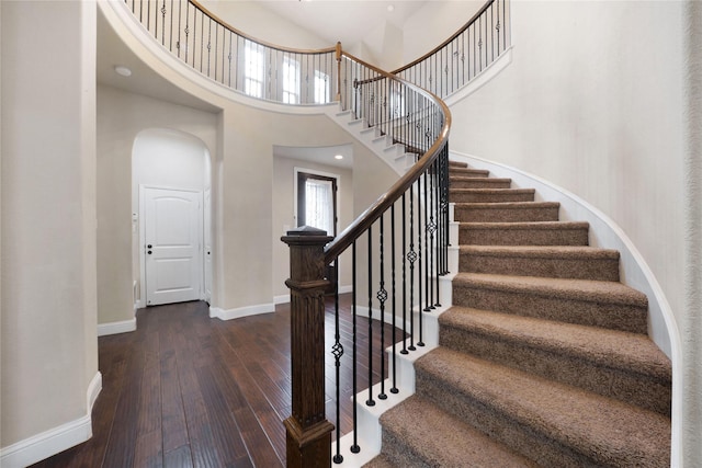 stairs with a high ceiling, wood-type flooring, baseboards, and arched walkways