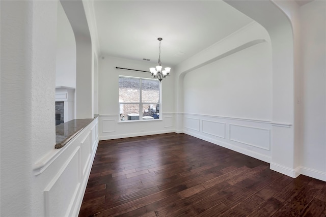 6917 Moody Ave, Frisco, TX 75035 - unfurnished dining area with a chandelier, dark wood-style flooring, wainscoting, arched walkways, and a fireplace