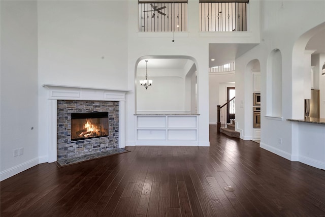 6917 Moody Ave, Frisco, TX 75035 - unfurnished living room with a tile fireplace, hardwood / wood-style floors, stairway, a towering ceiling, and arched walkways