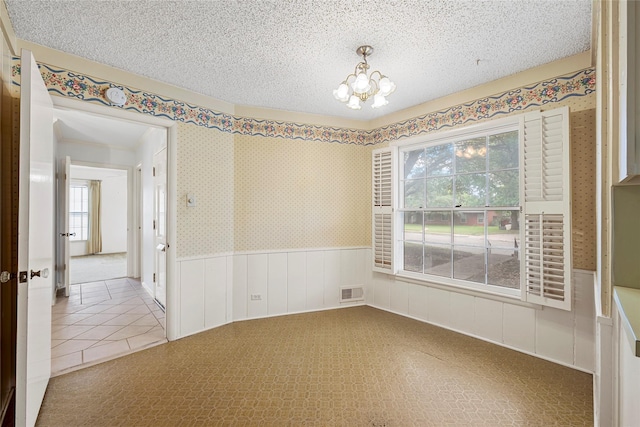spare room with visible vents, a textured ceiling, tile patterned floors, a wainscoted wall, and a notable chandelier