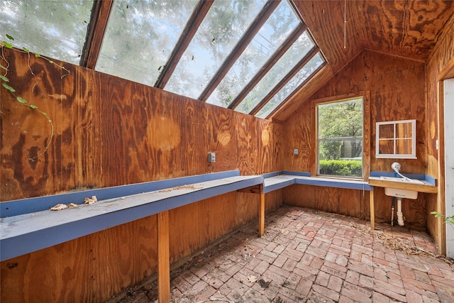 interior space featuring wooden walls, brick floor, and lofted ceiling with skylight