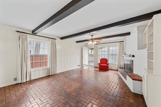 unfurnished living room with a decorative wall, brick floor, a brick fireplace, and beam ceiling