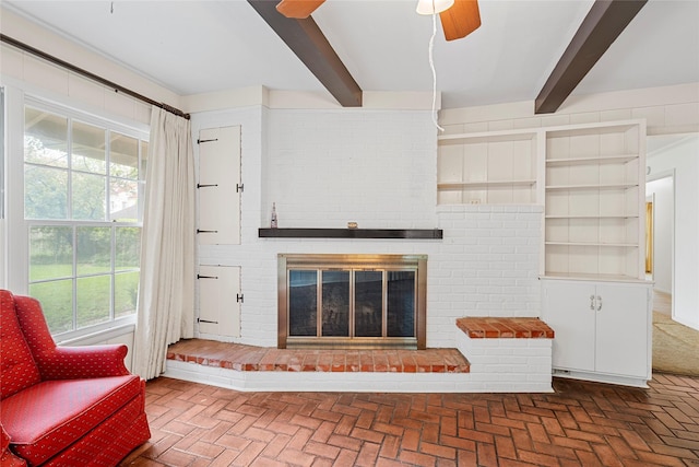 living room featuring brick floor, beam ceiling, a fireplace, and ceiling fan