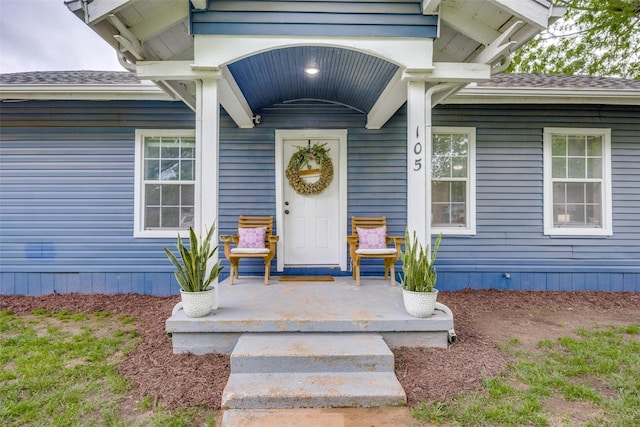 view of exterior entry with a porch and roof with shingles