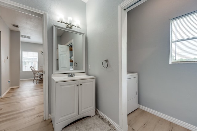 bathroom featuring vanity, baseboards, washer / dryer, wood finished floors, and visible vents