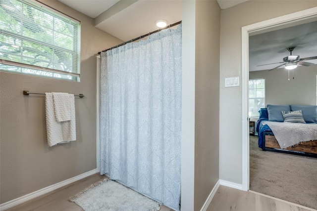 bathroom with wood finished floors, baseboards, ceiling fan, a shower with curtain, and ensuite bath