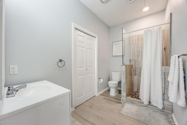 full bath with vanity, wood finished floors, toilet, baseboards, and a tile shower