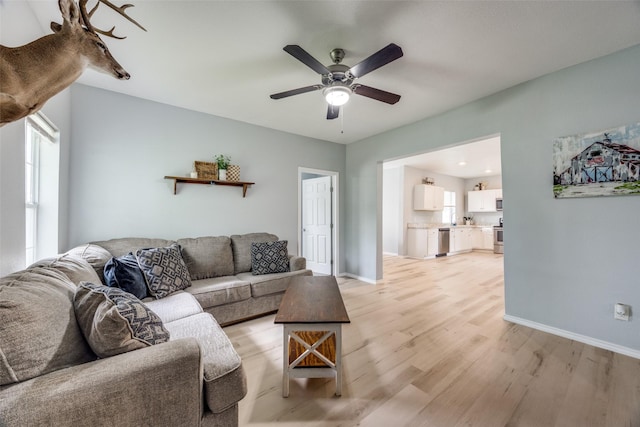 living area featuring a ceiling fan, baseboards, and light wood finished floors