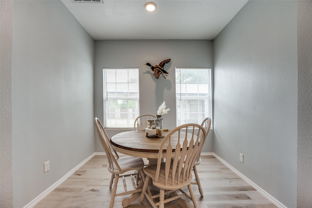 dining space featuring light wood-type flooring, baseboards, a textured wall, and visible vents