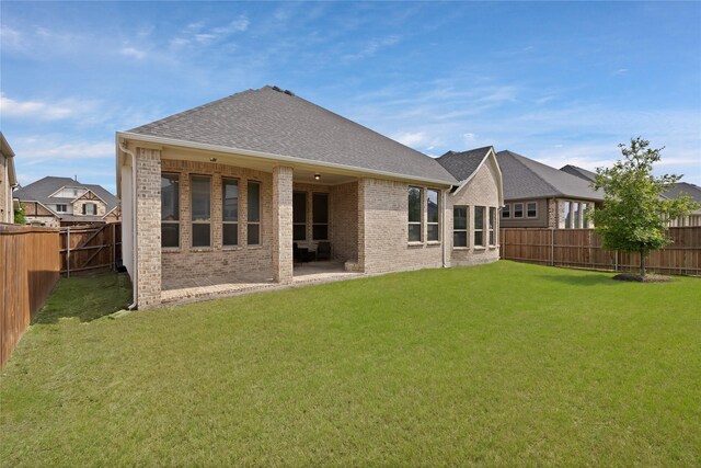 rear view of property featuring a fenced backyard, a shingled roof, a lawn, and brick siding