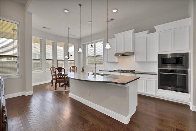 kitchen with visible vents, a center island with sink, dark stone counters, a sink, and stainless steel appliances