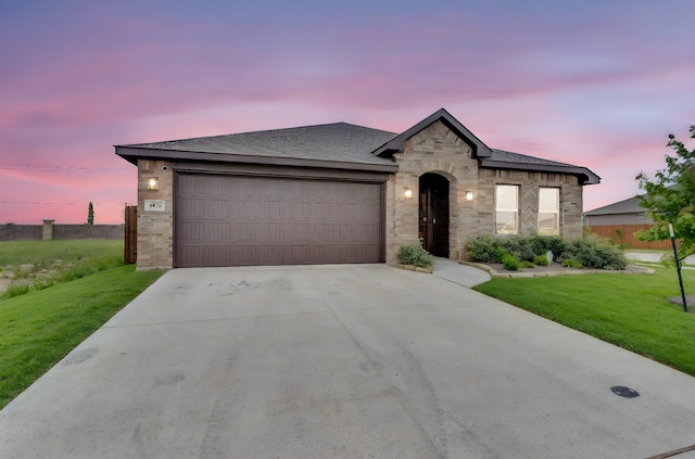 view of front of home featuring a lawn, a garage, stone siding, and concrete driveway
