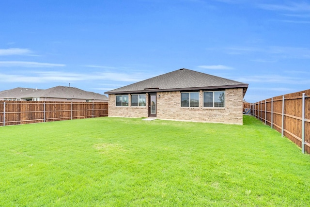 back of property featuring brick siding, a fenced backyard, roof with shingles, and a yard