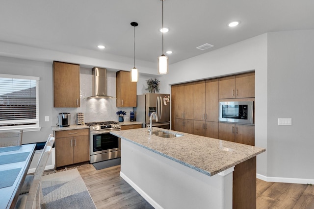 kitchen with visible vents, wall chimney range hood, light wood-type flooring, brown cabinets, and stainless steel appliances