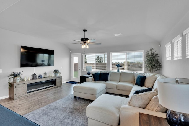 living area with a glass covered fireplace, a ceiling fan, baseboards, wood finished floors, and vaulted ceiling