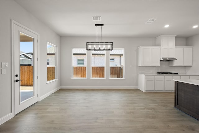 kitchen with a notable chandelier, light wood-style floors, white cabinetry, under cabinet range hood, and visible vents