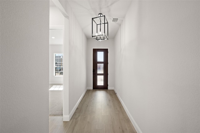 doorway with visible vents, light wood finished floors, baseboards, and a chandelier