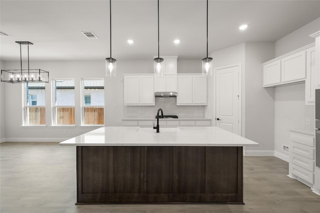 kitchen featuring light wood-style flooring, white cabinetry, baseboards, backsplash, and visible vents