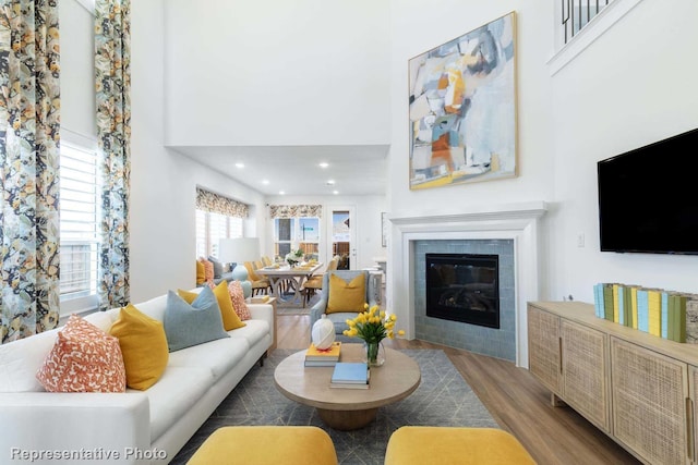 living area featuring a high ceiling, recessed lighting, a tile fireplace, and wood finished floors