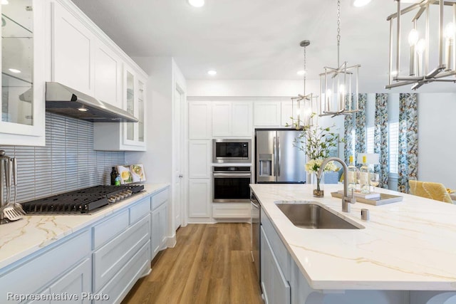 kitchen featuring appliances with stainless steel finishes, a sink, a chandelier, under cabinet range hood, and a center island with sink