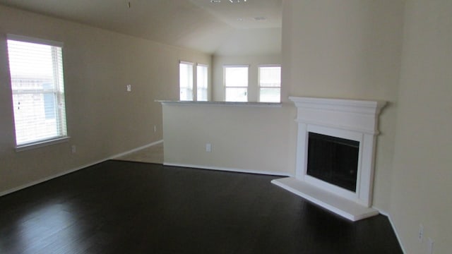 unfurnished living room featuring plenty of natural light, a fireplace with raised hearth, vaulted ceiling, and dark wood-type flooring