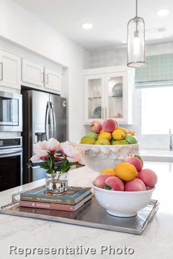 kitchen with pendant lighting, appliances with stainless steel finishes, light countertops, glass insert cabinets, and white cabinetry