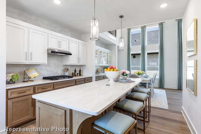 kitchen with a kitchen breakfast bar, decorative backsplash, gas stovetop, under cabinet range hood, and dark wood-style floors