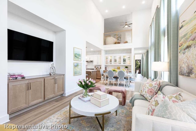 living area with a towering ceiling, baseboards, ceiling fan, recessed lighting, and light wood-style flooring