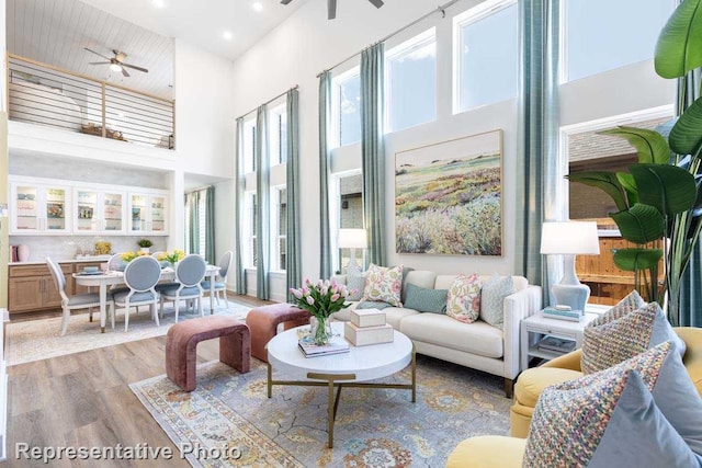living room featuring recessed lighting, a ceiling fan, light wood finished floors, and a towering ceiling