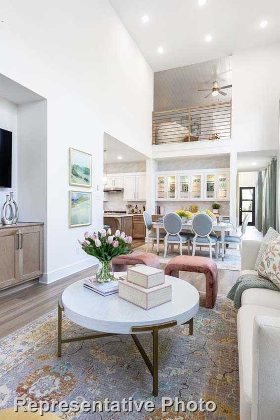 living room featuring light wood-style floors, baseboards, a high ceiling, recessed lighting, and a ceiling fan