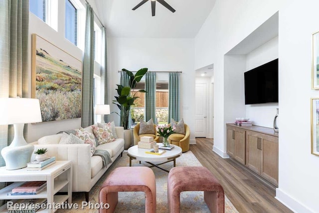 living room featuring a healthy amount of sunlight, a ceiling fan, wood finished floors, and a towering ceiling