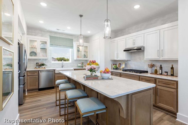 kitchen featuring a kitchen breakfast bar, a center island, under cabinet range hood, a sink, and appliances with stainless steel finishes