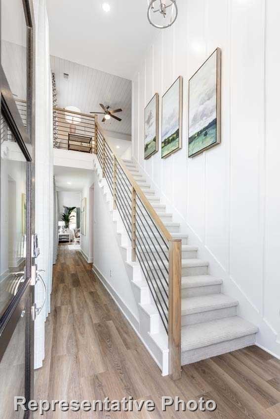 stairs featuring baseboards, a high ceiling, ceiling fan, and wood finished floors