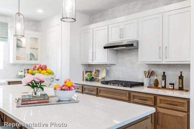 kitchen featuring backsplash, hanging light fixtures, light countertops, under cabinet range hood, and white cabinetry