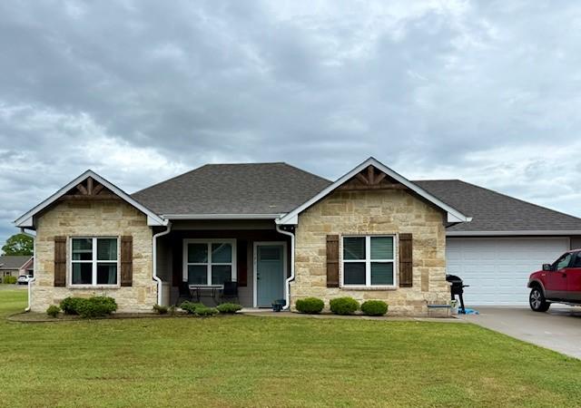 view of front of home with a front lawn, stone siding, an attached garage, driveway, and a porch