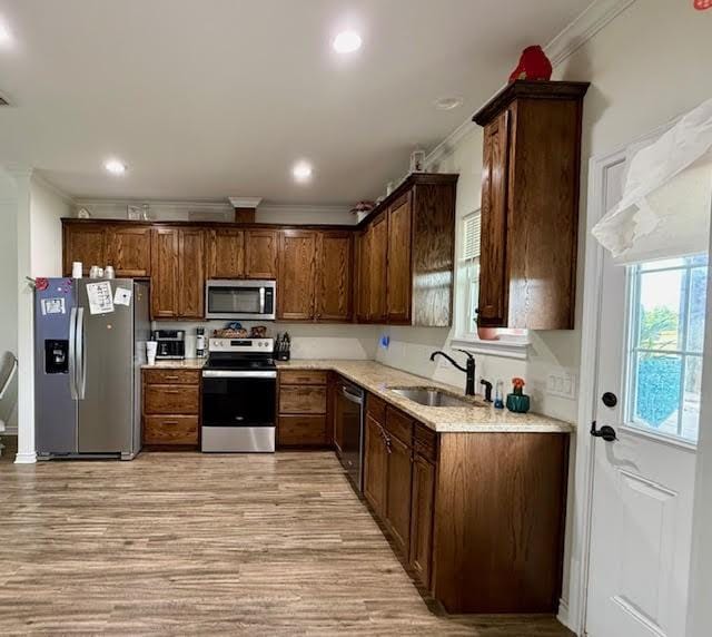 kitchen featuring crown molding, stainless steel appliances, a sink, and light wood-type flooring