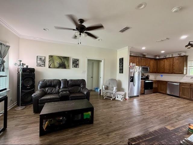 living room with visible vents, ornamental molding, ceiling fan, and dark wood-style floors