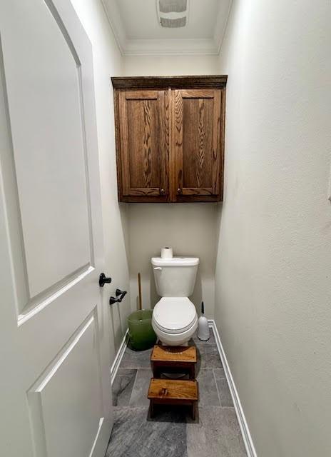bathroom featuring baseboards, crown molding, and toilet