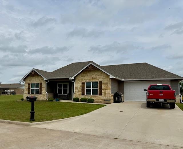 view of front of house with a garage, a front lawn, stone siding, roof with shingles, and concrete driveway
