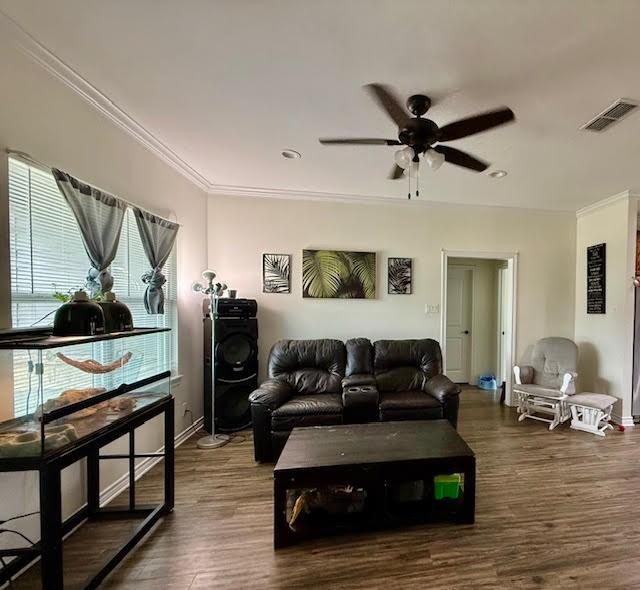 living area with crown molding, visible vents, wood finished floors, baseboards, and a ceiling fan