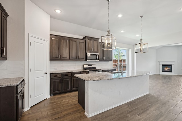 kitchen with dark brown cabinets, open floor plan, a sink, appliances with stainless steel finishes, and backsplash