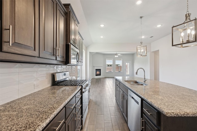 kitchen with backsplash, appliances with stainless steel finishes, wood finish floors, a sink, and ceiling fan with notable chandelier